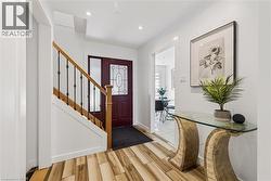 Inviting entryway featuring wood-finish flooring, a staircase with wood railing and iron balusters, a dark wood entry door with decorative glass, and recessed lighting - 