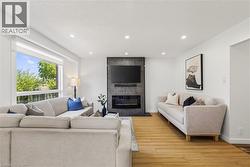 Living area featuring a modern linear fireplace with a textured dark gray surround, recessed ceiling lighting, a large picture window, and wood-finish flooring - 