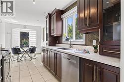 Kitchen featuring rich wood cabinetry, white countertops, a mosaic tile backsplash, stainless steel appliances, and a window above the sink - 