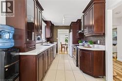 Galley kitchen featuring dark wood cabinetry with glass accents, white countertops, tile flooring, and a mosaic tile backsplash - 