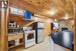 Wood-paneled room featuring a full kitchen setup with a white electric range, stainless steel refrigerator, and a dark countertop on a white base - 