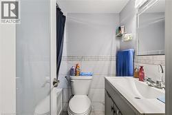 Bathroom featuring white subway tile, a vanity with an integrated sink, a wall-mounted mirror, and a commode - 