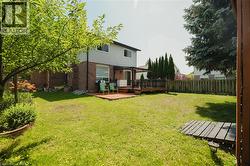 Expansive green lawn featuring a wooden deck with black railings, a partially covered patio area, and a brick and siding exterior - 