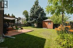 Expansive backyard featuring a wood-finish deck with a pergola, a manicured lawn, mature trees, and a wooden storage shed - 