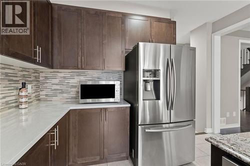 Kitchen featuring dark wood-finish cabinetry, light-toned countertops, a mosaic tile backsplash, and stainless steel appliances - 96 Damselfly Way, Ottawa, ON - Indoor Photo Showing Kitchen With Upgraded Kitchen