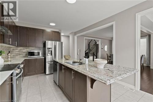 Contemporary kitchen featuring a spacious island with a light-toned countertop, a double basin sink, and dark wood-finish cabinetry - 96 Damselfly Way, Ottawa, ON - Indoor Photo Showing Kitchen With Double Sink With Upgraded Kitchen