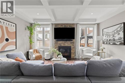 Living room featuring a stacked stone fireplace with a built-in television mount, coffered ceilings with recessed lighting, and large windows with white trim - 96 Damselfly Way, Ottawa, ON - Indoor Photo Showing Living Room With Fireplace