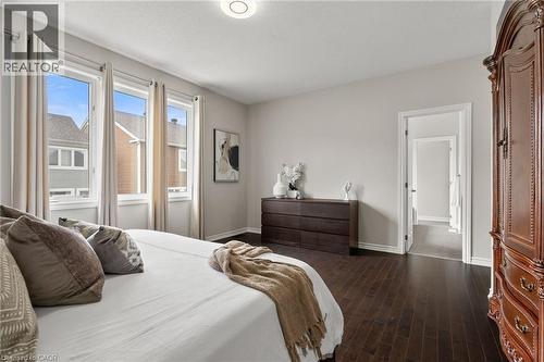 Spacious room featuring dark wood-finish flooring, light neutral wall paint, and multiple windows with cream-colored drapes - 96 Damselfly Way, Ottawa, ON - Indoor Photo Showing Bedroom
