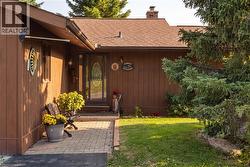 Brown siding exterior with a shingle roof, featuring a glass panel entry door, a brick paver pathway, and established evergreen landscaping - 