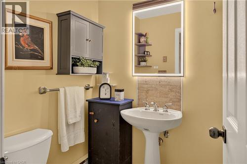 Pedestal sink with chrome faucet, illuminated mirror, and stone-tile backsplash - 12613 Second Line, Milton, ON - Indoor Photo Showing Bathroom