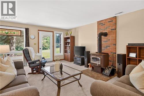 Living area featuring a brick accent wall with a wood-burning stove, white trim, stained glass window detail, and access to exterior - 12613 Second Line, Milton, ON - Indoor Photo Showing Living Room