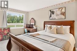 Bedroom featuring a large picture window, a wood-finish bed frame with a carved headboard, light neutral wall paint, and carpeted flooring - 