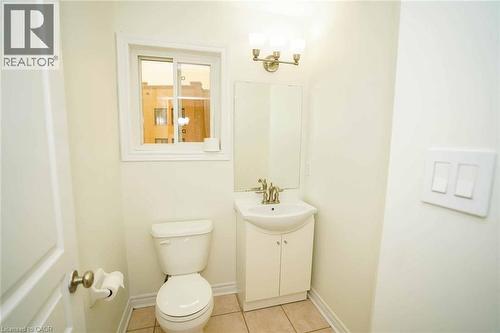 Bathroom featuring a white vanity with integrated sink, a toilet, a window with white trim, and a three-light vanity fixture - 18 Heritage Drive, Guelph, ON - Indoor Photo Showing Bathroom