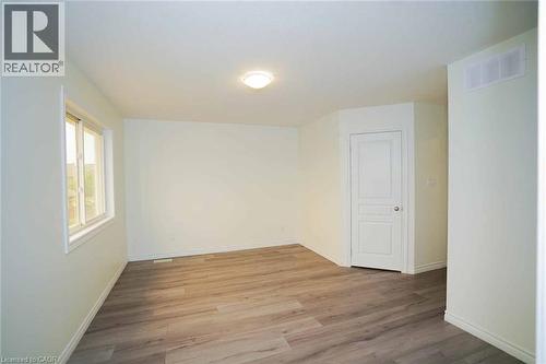 Spacious interior featuring wood-finish flooring, light-colored walls, white trim, a double-paned window, and a flush-mount ceiling light fixture - 18 Heritage Drive, Guelph, ON - Indoor Photo Showing Other Room