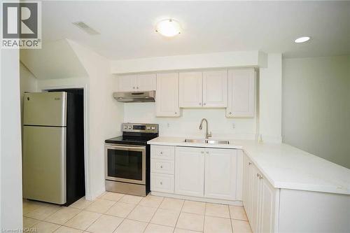 Kitchen featuring white cabinetry, light-toned countertops, a stainless steel range with overhead ventilation, and a stainless steel refrigerator - 18 Heritage Drive, Guelph, ON - Indoor Photo Showing Kitchen