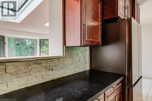 Kitchen featuring dark wood cabinetry, a built-in stainless steel refrigerator, black speckled countertops, and a stacked stone backsplash - 109 White Oak Place, Waterloo, ON - Indoor Photo Showing Kitchen