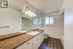 Bathroom featuring a double vanity with stone-look countertops, integrated sinks, white cabinetry, and wood-finish flooring - 