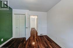 Room featuring rich wood-finish flooring, white baseboards, a bi-fold closet, and a hallway entry - 