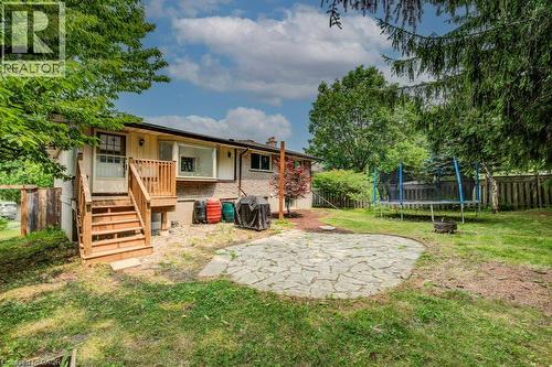 Expansive rear yard featuring a stone paver patio, mature perimeter trees, and a wooden deck with stairs providing outdoor access - 109 White Oak Place, Waterloo, ON - Outdoor