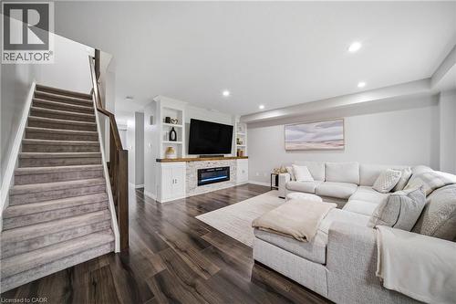 Finished lower level featuring wood-finish flooring, a built-in media console with shelving and base cabinets, an integrated electric fireplace with stone-look surround, recessed lighting, and a carpe - 750 Lawrence Street Unit# 38, Cambridge, ON - Indoor Photo Showing Living Room With Fireplace