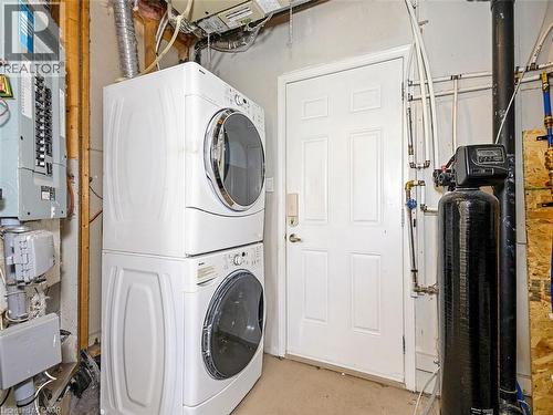 Laundry area featuring a stacked washer and dryer, an electrical panel, a water softener system, and a utility door - 656 Frank Place, Milton, ON - Indoor Photo Showing Laundry Room