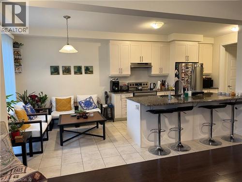 Open-concept kitchen and living area featuring a large island with seating, stainless steel appliances, white cabinetry, and a combination of tile and wood-finish flooring - 63 Ridge Road, Cambridge, ON - Indoor Photo Showing Kitchen With Double Sink