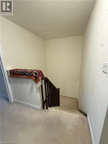 Carpeted staircase with dark wood-finish handrail and balusters, featuring a light beige wall and matching carpet flooring - 63 Ridge Road, Cambridge, ON - Indoor Photo Showing Other Room