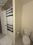 Bathroom featuring a white panel door, tiled flooring, a bathtub with a tiled surround, and a white toilet - 