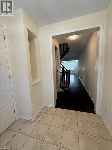 Entryway featuring light-toned square tile flooring, a built-in wall niche, and an archway opening to a hallway with dark wood-finish flooring and a staircase with black railings - 63 Ridge Road, Cambridge, ON - Indoor Photo Showing Other Room
