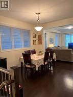 Open-concept dining area featuring dark wood-finish flooring, a contemporary pendant light fixture, and large windows with horizontal blinds - 