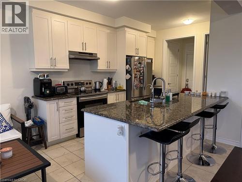 Kitchen featuring white cabinetry, stainless steel appliances, a multi-tone granite countertop island with integrated sink, and tiled flooring - 63 Ridge Road, Cambridge, ON - Indoor Photo Showing Kitchen
