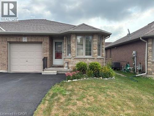 Stone and brick-clad exterior featuring a single-car garage with a light-colored door, a paved driveway, and a front entry with a small porch and bay window - 49 Millcroft Drive, Simcoe, ON - Outdoor