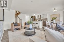 Open-concept living space featuring wood-finish flooring, a contemporary kitchen with a peninsula island, a designated dining area, and a staircase with wood risers and banister - 