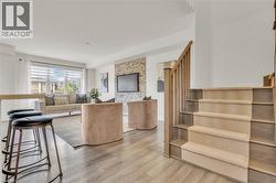 Open-concept living space featuring wood-finish flooring, a contemporary staircase with carpeted treads, a large window with horizontal blinds, and a stone accent wall - 