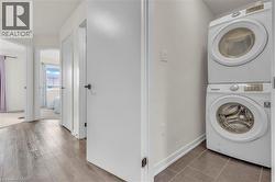 Hallway with wood-finish flooring leading to multiple rooms, featuring a dedicated laundry area with stacked white appliances on tile flooring - 