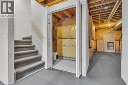 Carpeted staircase with a wood handrail, contrasting with the unfinished area featuring exposed ceiling joists and insulation - 