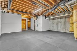 Expansive basement space featuring a grey interlocking floor, exposed wood joist ceiling, and concrete foundation walls - 