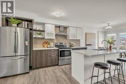 Modern kitchen featuring an island with a stainless steel sink, stainless steel appliances, wood-finish flooring, two-tone cabinetry, and a tile backsplash - 