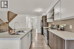 Bright kitchen featuring an island with a double stainless steel sink, light-toned countertops, and wood-finish flooring - 