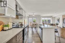 Open-concept kitchen with light wood-finish flooring, white cabinetry with frosted glass inserts, stainless steel appliances, and a central island with a breakfast bar - 