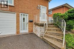 Brick exterior featuring a white garage door, white entry door with decorative glass, concrete steps with white metal railings, and established perimeter shrubbery - 