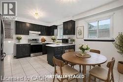 Kitchen featuring dark cabinetry, stainless steel appliances, a white tile backsplash, a center island with countertop, and light-toned floor tiling - 