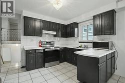 Kitchen featuring dark cabinetry, white square tile flooring, white subway tile backsplash, and a stainless steel electric range - 