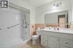 Bathroom featuring a white vanity with integrated sink, a large wall-mounted mirror, and a shower with grab bars and a handheld showerhead - 