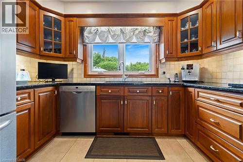 U-shaped kitchen featuring wood cabinetry, dark countertops, a stainless steel dishwasher, and light tile flooring - 7 Thomson Road, Simcoe, ON - Indoor Photo Showing Kitchen