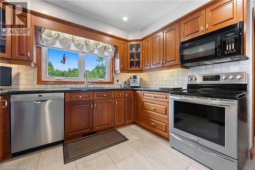 Kitchen featuring cherry wood cabinetry, stainless steel appliances, a black countertop, and a tiled backsplash - 7 Thomson Road, Simcoe, ON - Indoor Photo Showing Kitchen