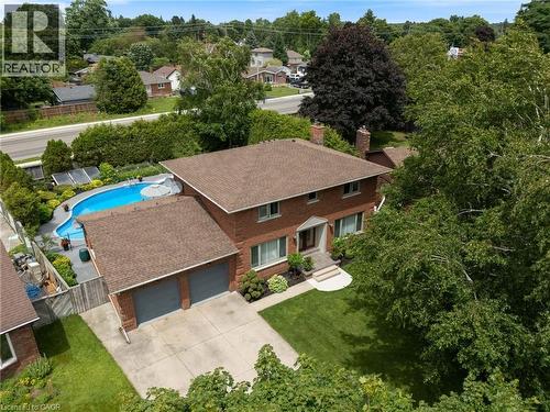 Brick exterior residence featuring a two-car garage, mature landscaping, a paved driveway, and an in-ground swimming pool - 7 Thomson Road, Simcoe, ON - Outdoor