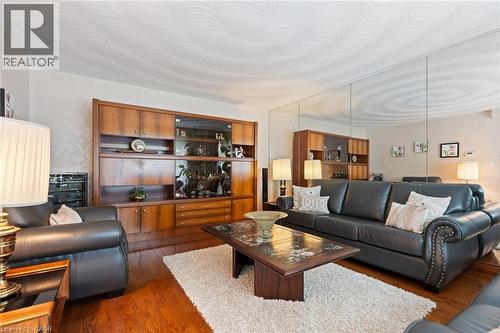 Living area featuring wood-finish flooring, a wall-mounted built-in cabinet with glass-front display, and a full-wall mirror accent - 7 Thomson Road, Simcoe, ON - Indoor Photo Showing Living Room