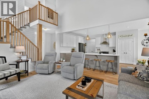 Vaulted ceiling living space featuring a stairway with wood balusters, wood-finish flooring, a kitchen island with seating, and pendant lighting - 87 Boyd Boulevard, Thamesford, ON - Indoor Photo Showing Living Room