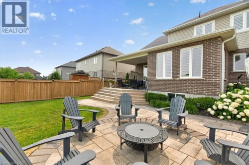 Expansive paved patio with a fire pit, bordered by a manicured lawn and a wooden privacy fence - 87 Boyd Boulevard, Thamesford, ON - Outdoor With Deck Patio Veranda With Exterior